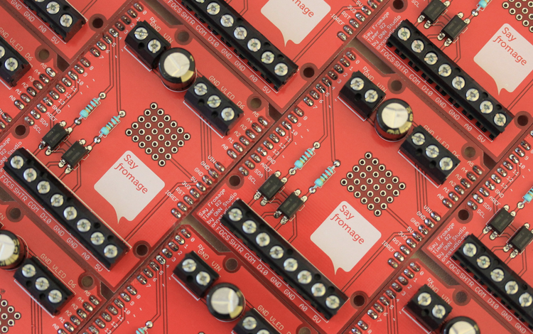 An array of custom red Say Fromage circuit boards, with chips, resistors and screw terminals.